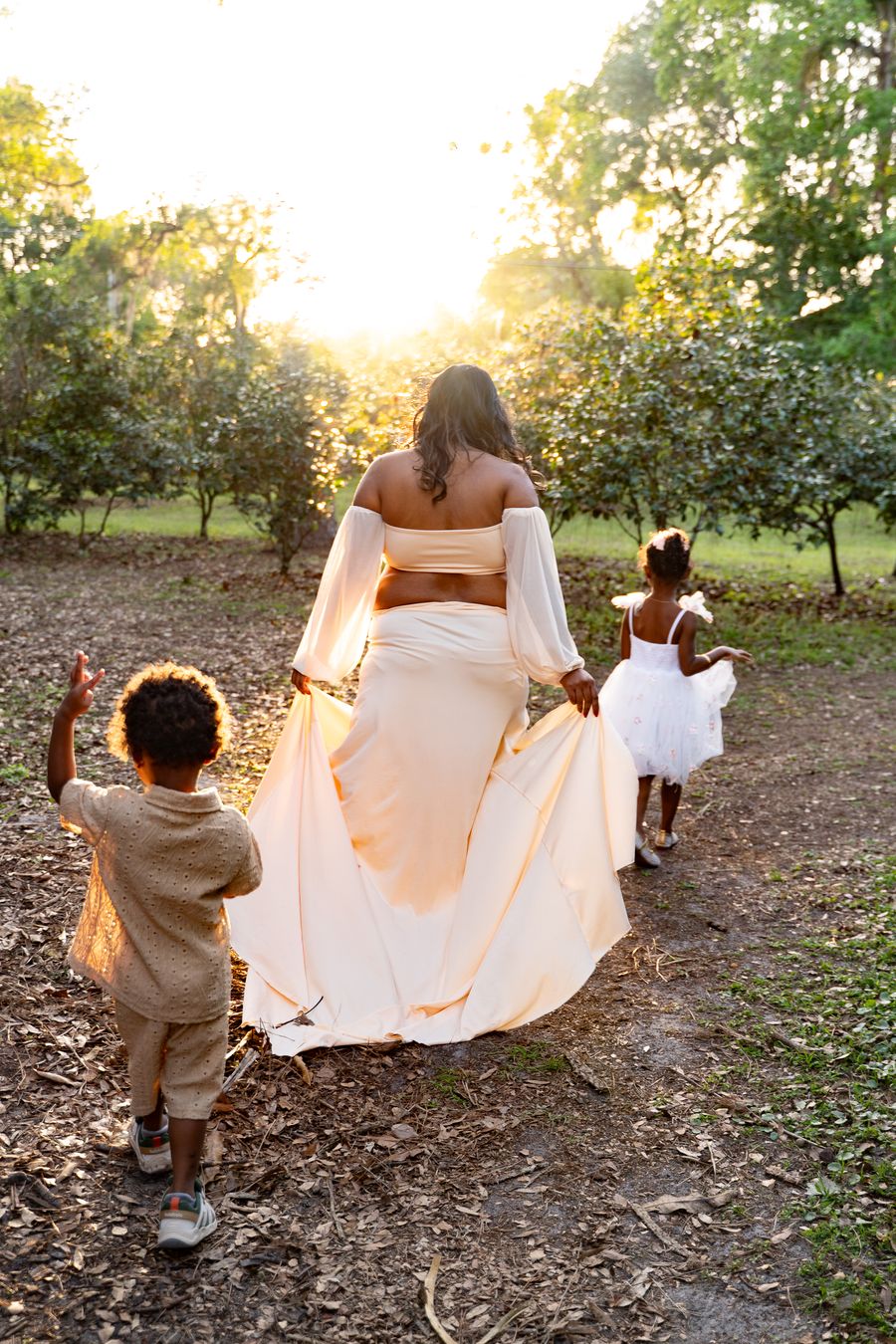 Mother walking with two children through a sunlit orchard