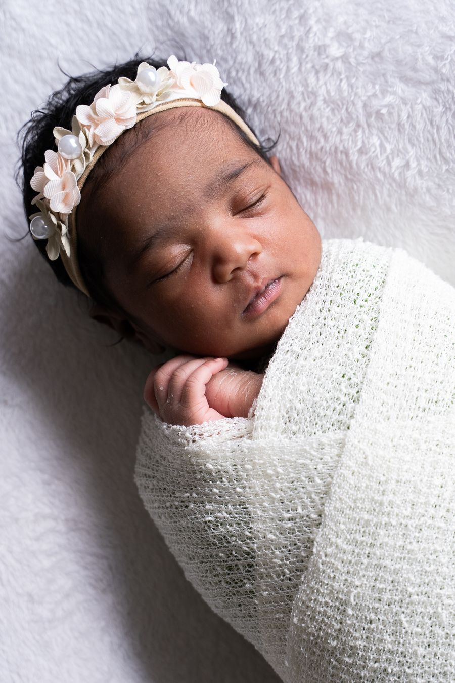 Sleeping newborn in a floral headband wrapped in a soft knit blanket